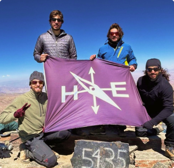 Foto de 4 pessoas da equipe Habitat segurando uma bandeira com o logo da Habita Expedições